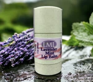 Green tube of lip balm with purple lavender and green mint leaves in the background.